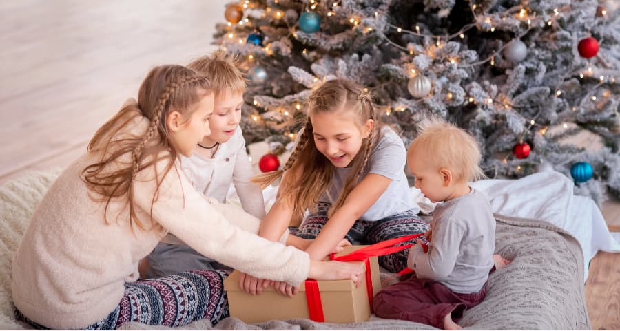 Siblings opening a gift in the living room beside a Christmas tree.